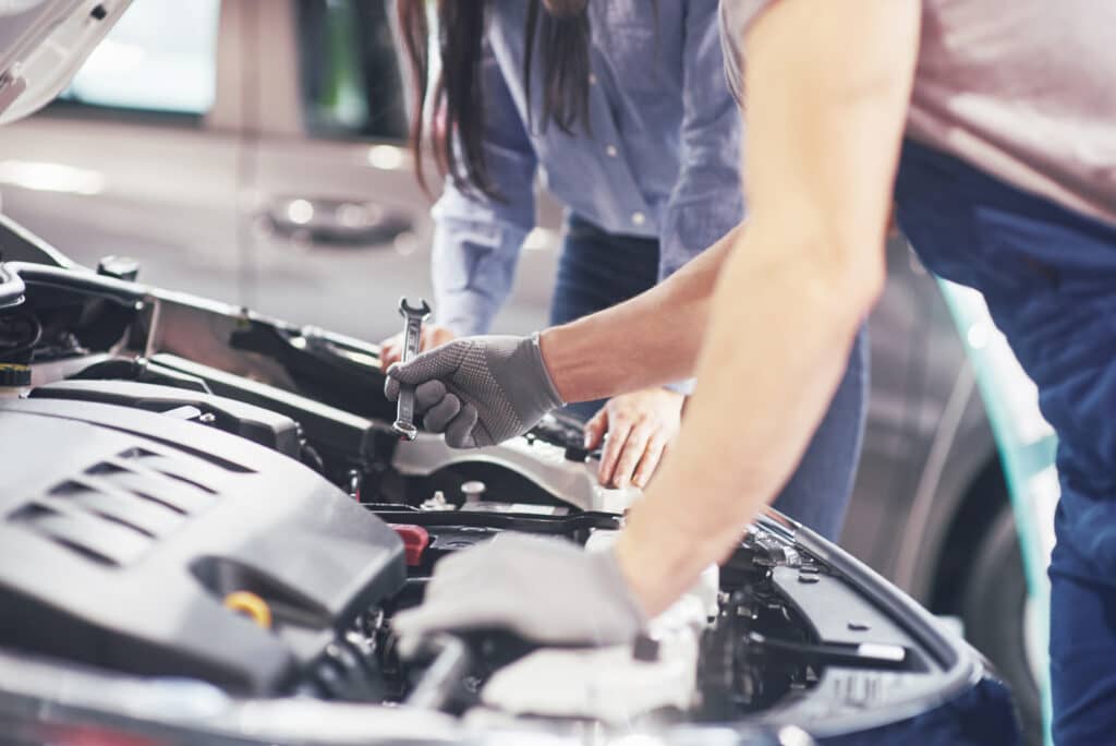 A man mechanic and woman customer look at the car hood and discuss repairs.